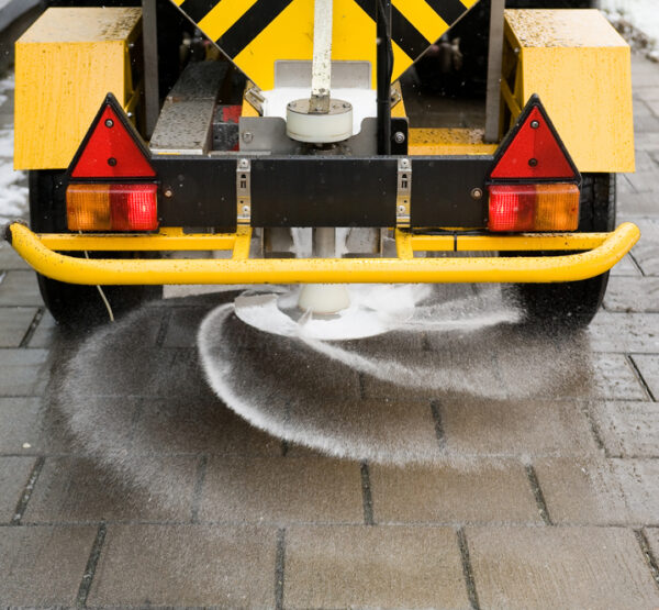 A machine is sprinkling salt on a sidewalk